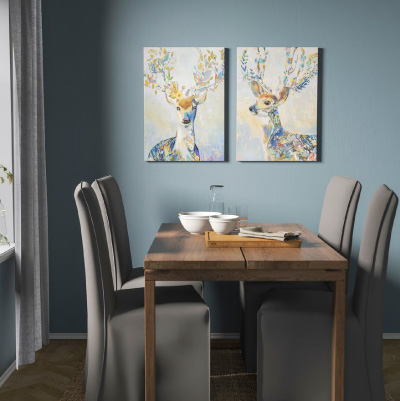 Salle à manger décorée de deux tableaux colorés représentant des cerfs, illustrant l'utilisation d'images animalières comme objets décoratifs.
